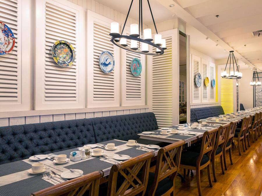 Una larga mesa de comedor con múltiples sillas, un banco acolchado azul y una fila de platos decorativos en la pared.