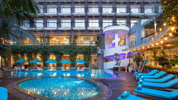 A hotel with a pool, lounge chairs, and a covered area with umbrellas. - THE 1O1 Bogor Suryakancana (Bogor)