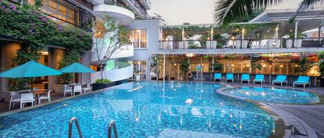 A hotel pool area with a large central pool, lounge chairs, and umbrellas.