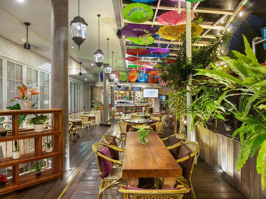 A restaurant with wooden tables and chairs, hanging umbrellas, and potted plants.
