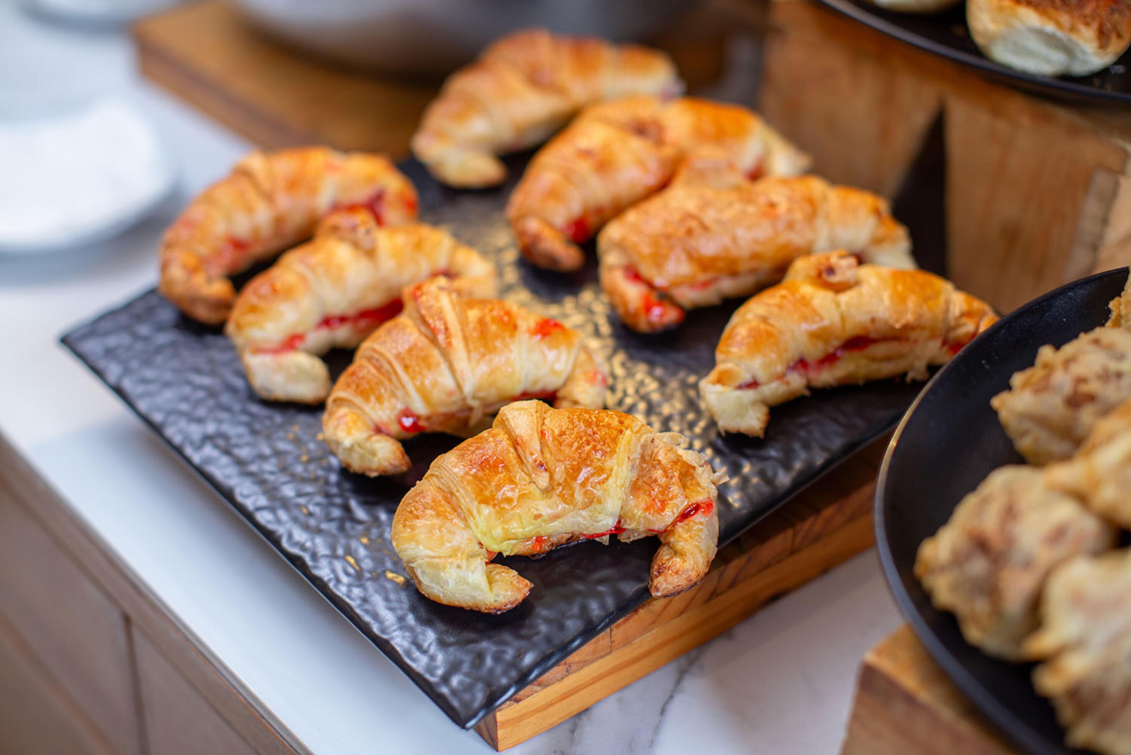 A tray of golden-brown croissants with visible red fruit filling, placed on a dark slate serving board.