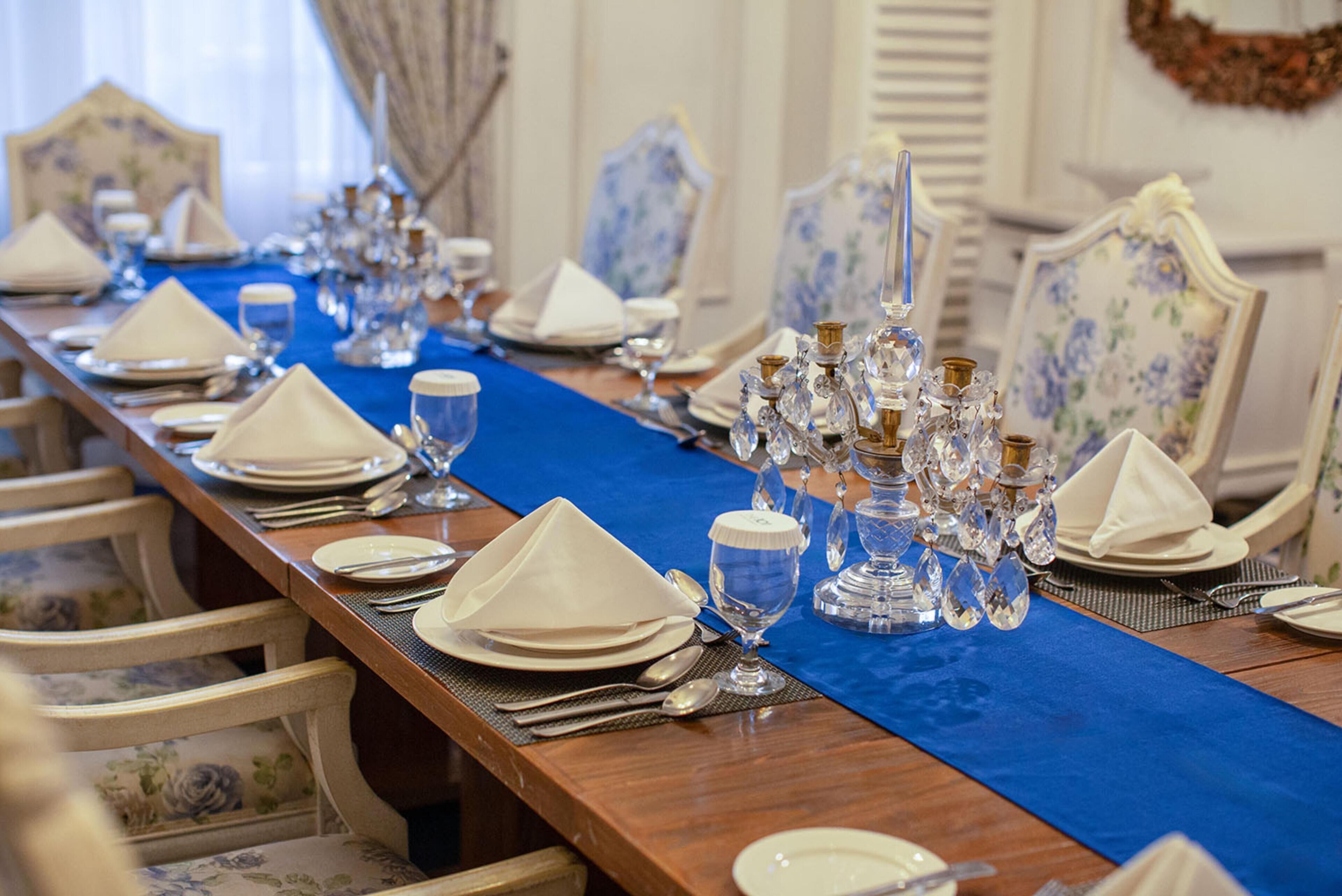 Una mesa de comedor formal con servilletas blancas, cubiertos y cristalería, flanqueada por sillas con estampado floral.