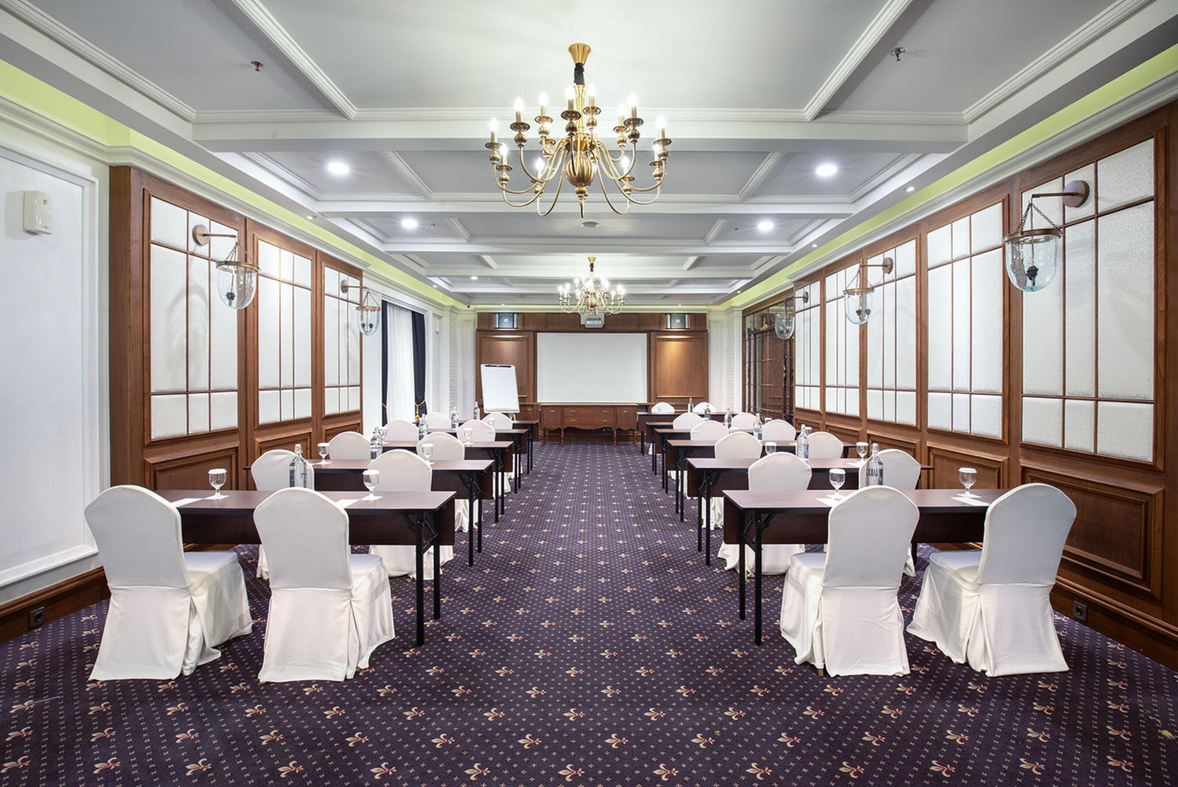 A conference room with a long table, chairs, a projector screen, and a chandelier.