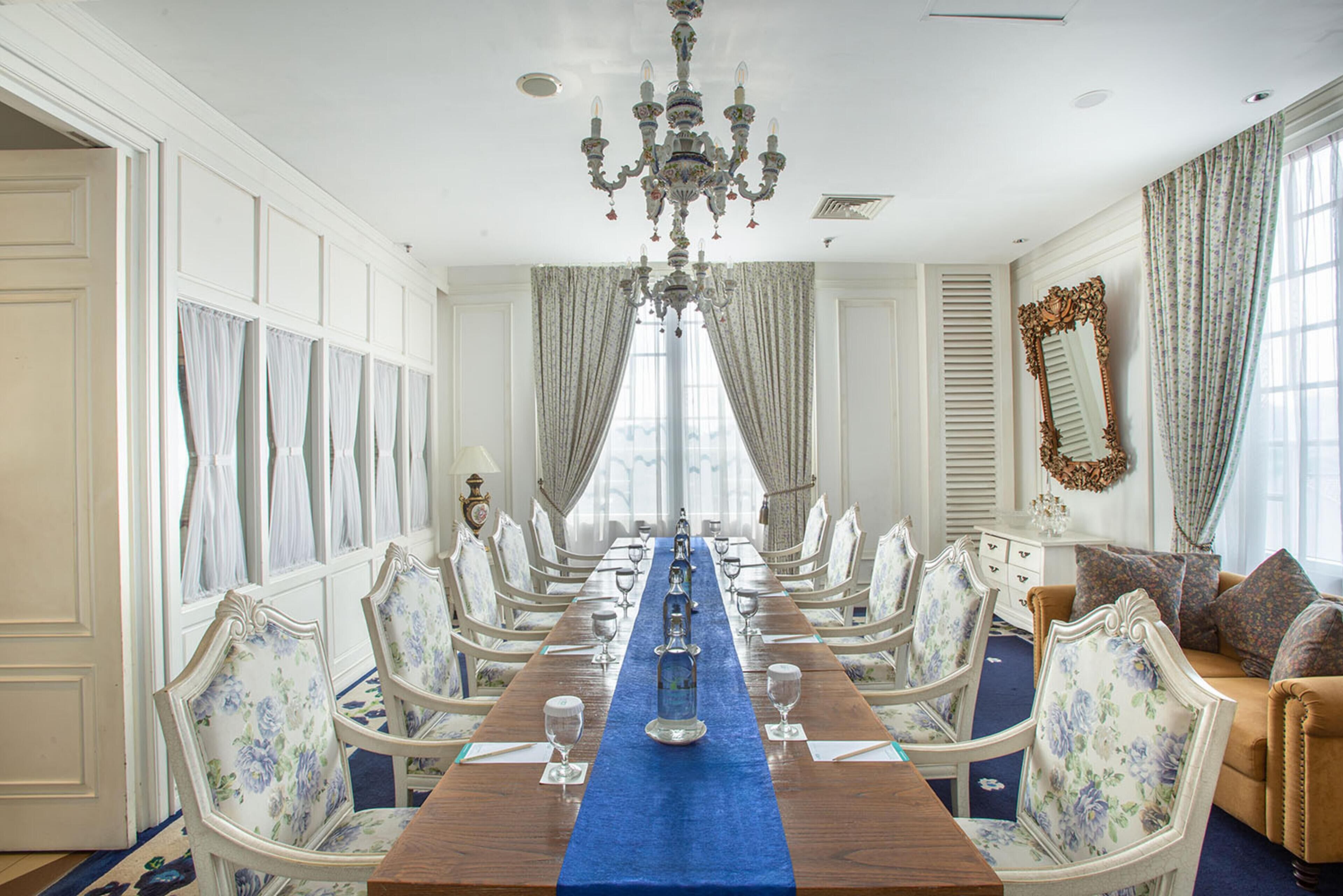 Une salle à manger élégante, avec une longue table, des chaises richement décorées et un lustre.