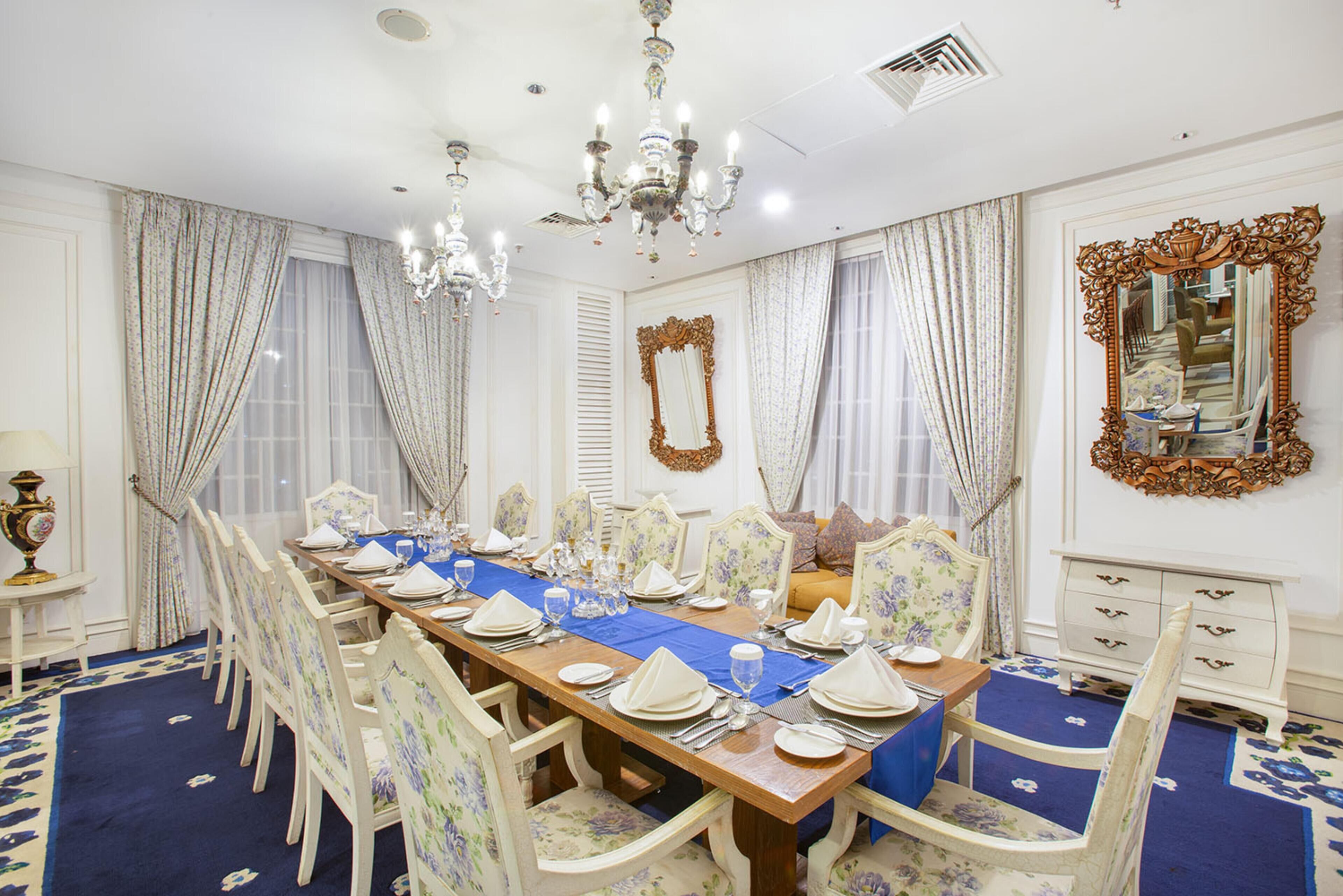 A formal dining room with a long table set for a meal, surrounded by chairs.