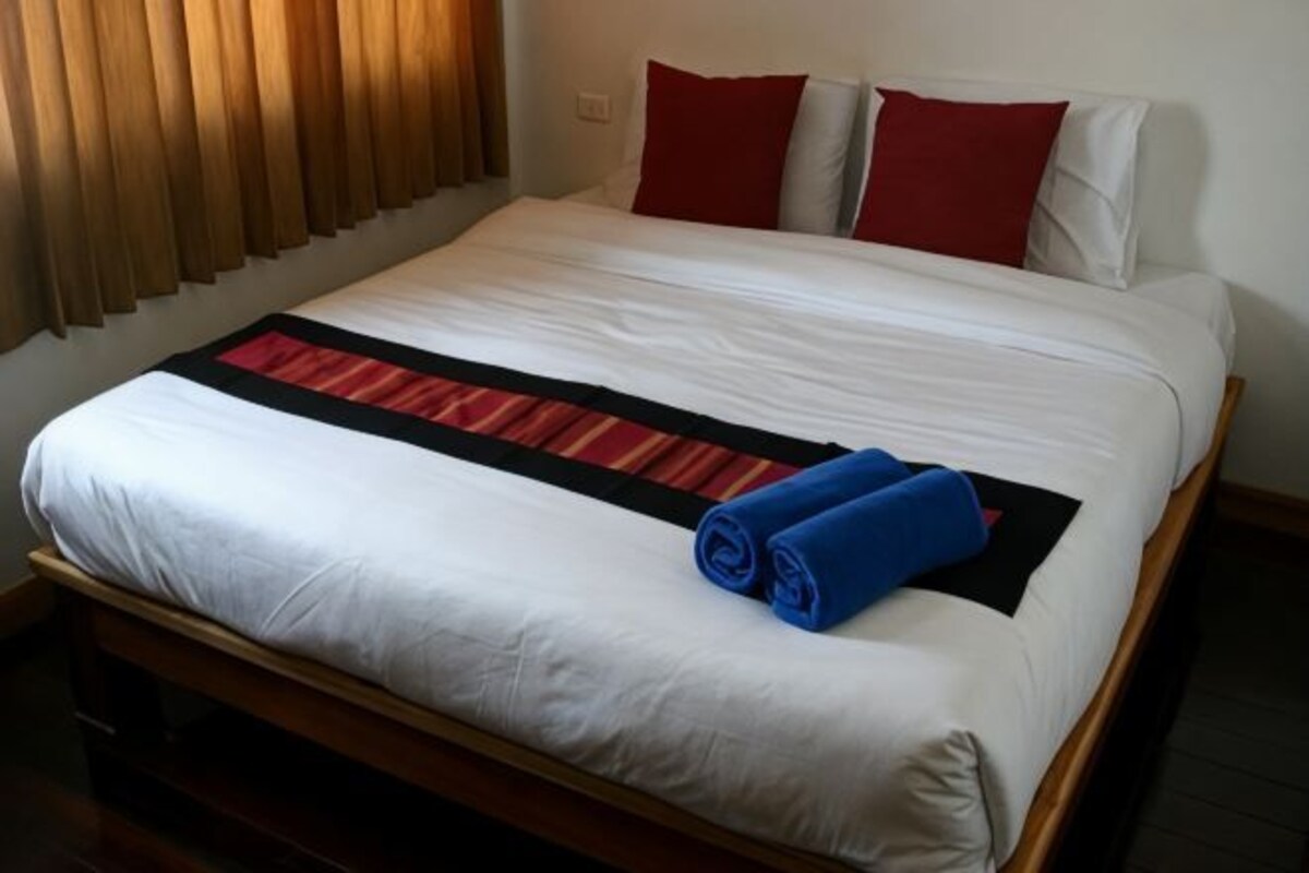 Una cama bien hecha con una colcha blanca y roja, una toalla azul enrollada y dos almohadas rojas.