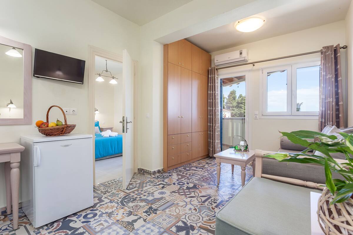 A compact kitchen with a refrigerator, wooden cabinets, a small table, and a sofa.