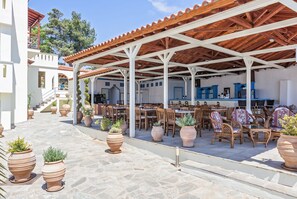 Un espace extérieur aménagé en terrasse, avec plusieurs tables et chaises, entouré de pots en terre cuite et de plantes en pot.