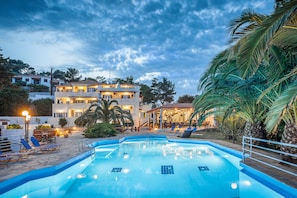 Une piscine avec des chaises longues, un espace de détente couvert et un bâtiment doté de plusieurs balcons en arrière-plan.