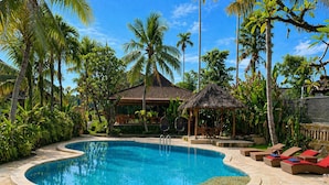 A swimming pool with a curved edge, surrounded by palm trees and a thatched-roof structure. - Saren Indah Hotel (Ubud)