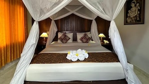 A bed with a canopy, pillows, a bedside table with a lamp, and a wall-mounted phone. - Saren Indah Hotel (Ubud)