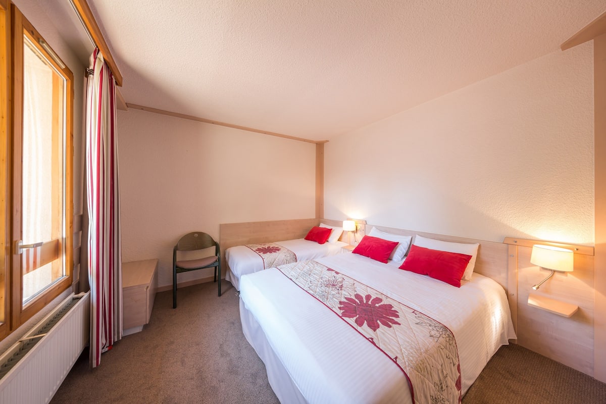 Une chambre d’hôtel avec deux lits, une chaise, une table de chevet et une fenêtre avec des rideaux.