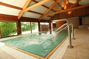 Una piscina interior con agua cristalina, vigas de madera y suelo de baldosas.