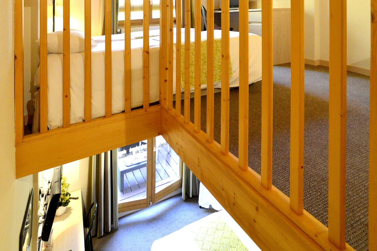 Une pièce avec un plafond en bois, un lit, un bureau avec une chaise et une fenêtre avec des rideaux.