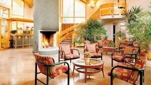 Een ruime lobby met een hoge plafond, houten balken, een centraal gelegen openhaard en comfortabele zithoeken.