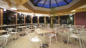 Een ruime eetruimte met houten balken, witte stoelen en tafels.