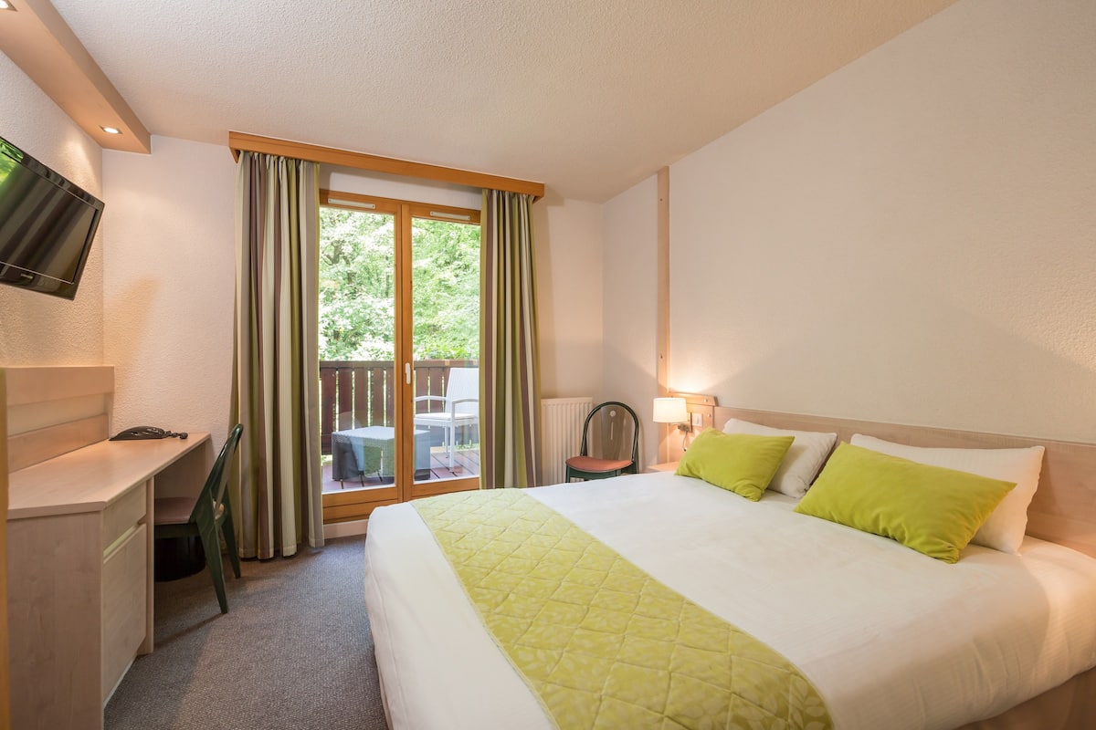 Une chambre d’hôtel équipée d’un lit, d’un bureau, d’une chaise, d’une télévision et offrant une vue sur l’extérieur.