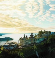 A traditional multi-story building with a central courtyard, surrounded by lush greenery and overlooking a body of water.