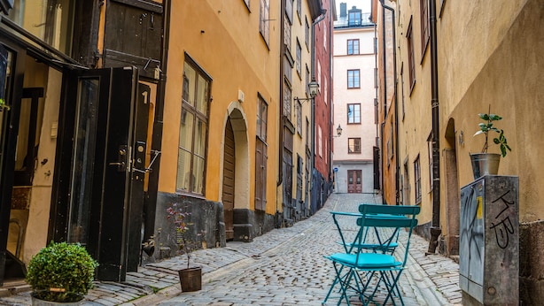 A cobblestone street with a narrow alley, a blue chair, and a potted plant. - Archipelago Hostel Old Town (Stockholm)
