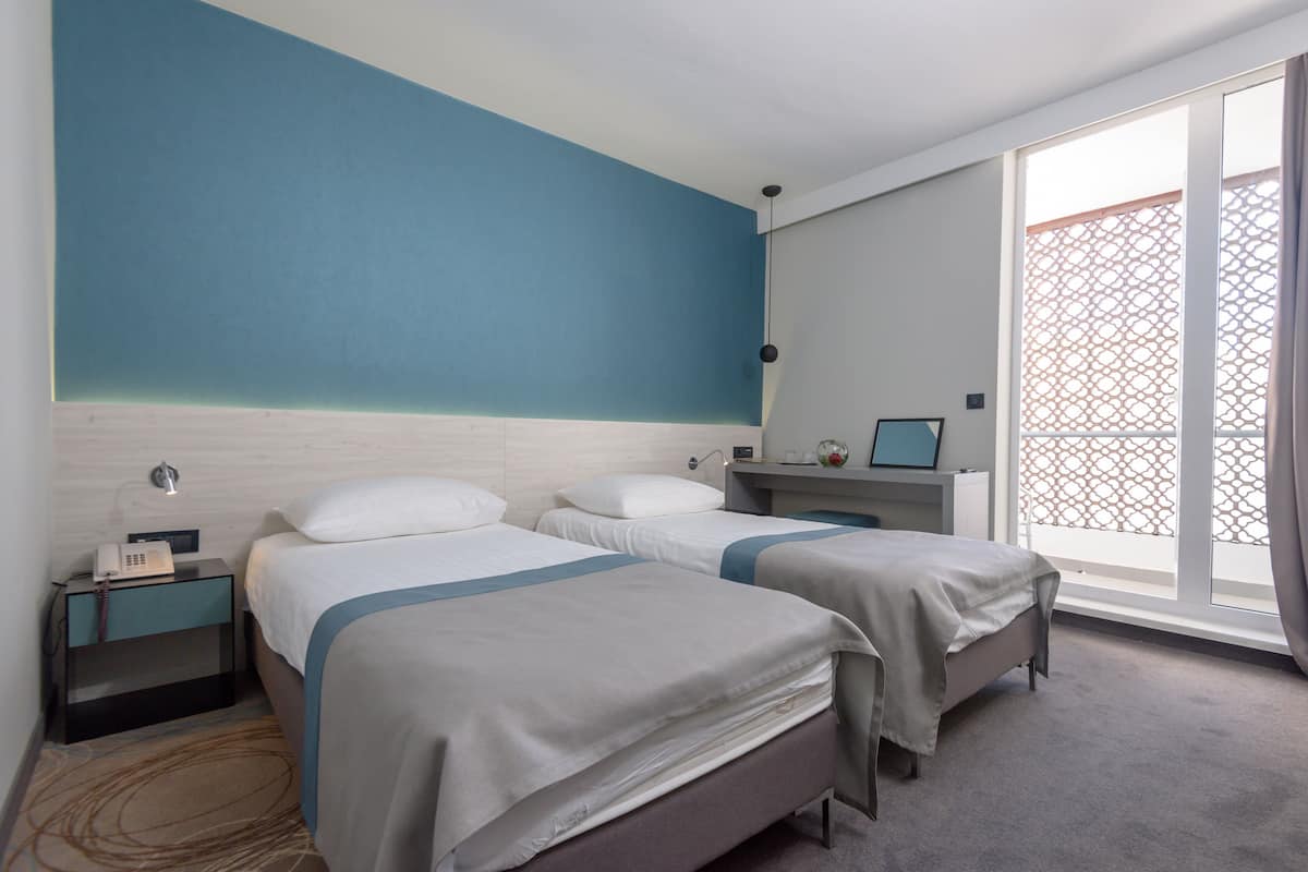 A hotel room with two beds, a desk, a nightstand, and a large window with a view.