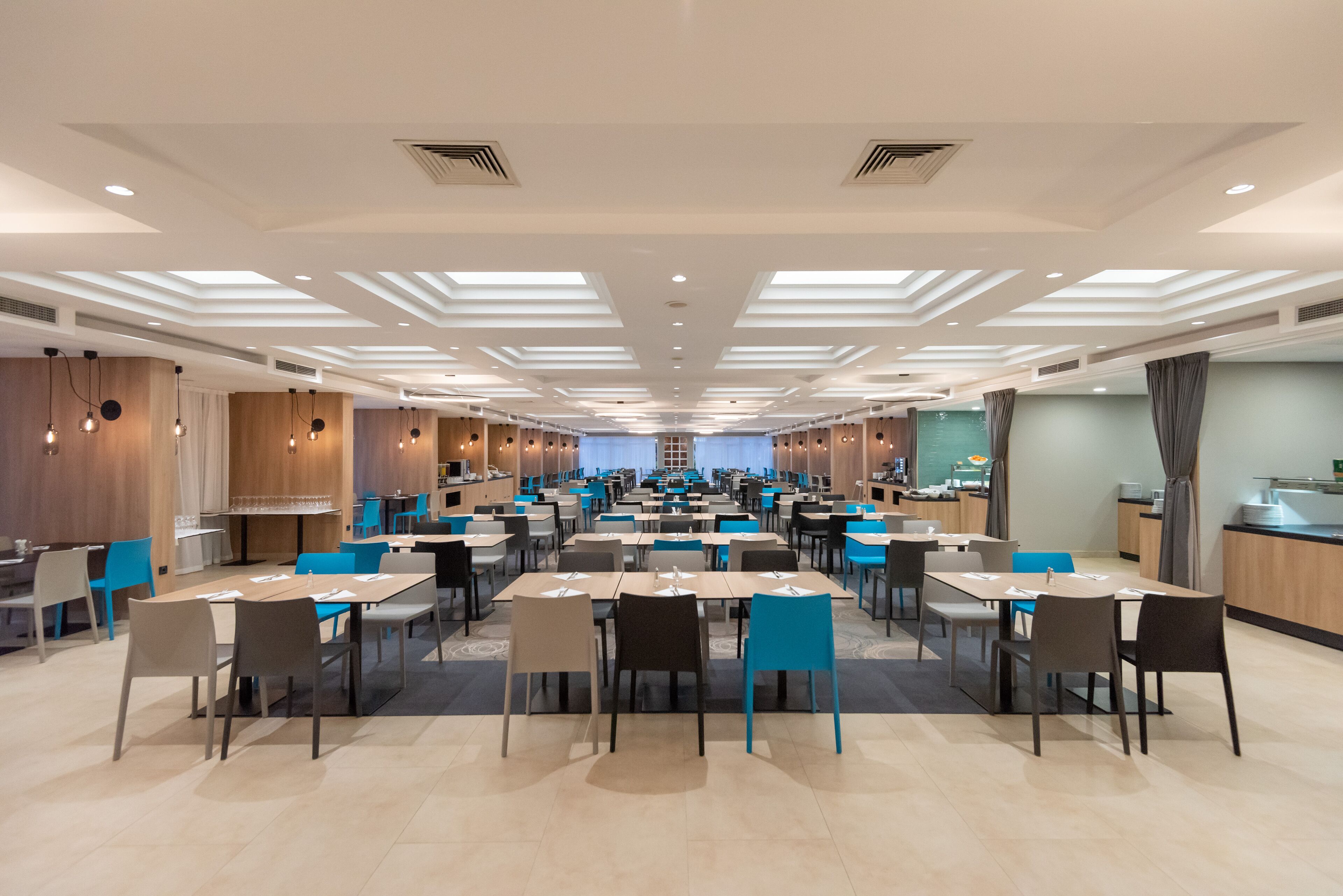 Un vaste espace dédié à la salle à manger, avec de nombreuses tables et chaises, des spots encastrés au plafond et une allée centrale.