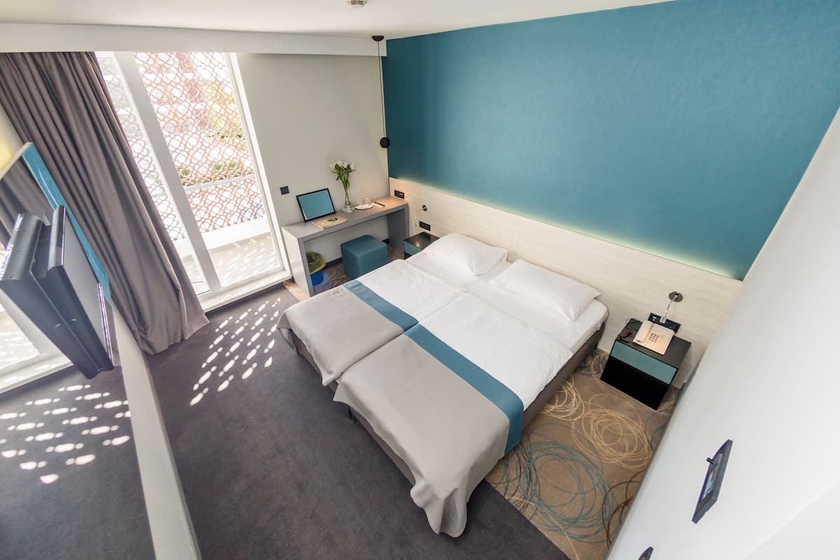 A modern hotel room with a bed, desk, and a view of the outdoors.