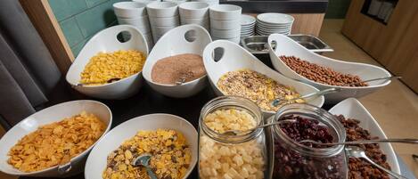 Un bufé de desayuno con diversos cereales y complementos en cuencos y frascos.