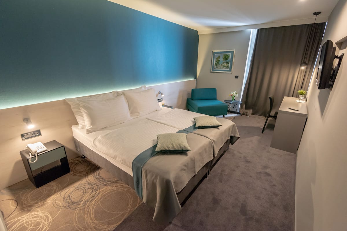 A hotel room with a large bed, a desk, a chair, a small table, and a mirror.