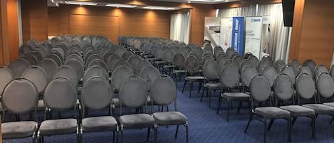 A conference room with rows of grey chairs, a blue carpet, and a ceiling with recessed lighting.