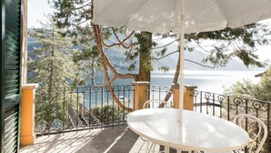 A balcony with a white table and umbrella, overlooking a lake and mountains. - Villa Nina Relais Boutique B&B (Carate Urio)