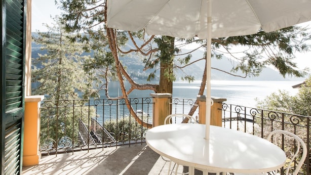 A balcony with a white table and umbrella, overlooking a lake and mountains. - Villa Nina Relais Boutique B&B (Carate Urio)