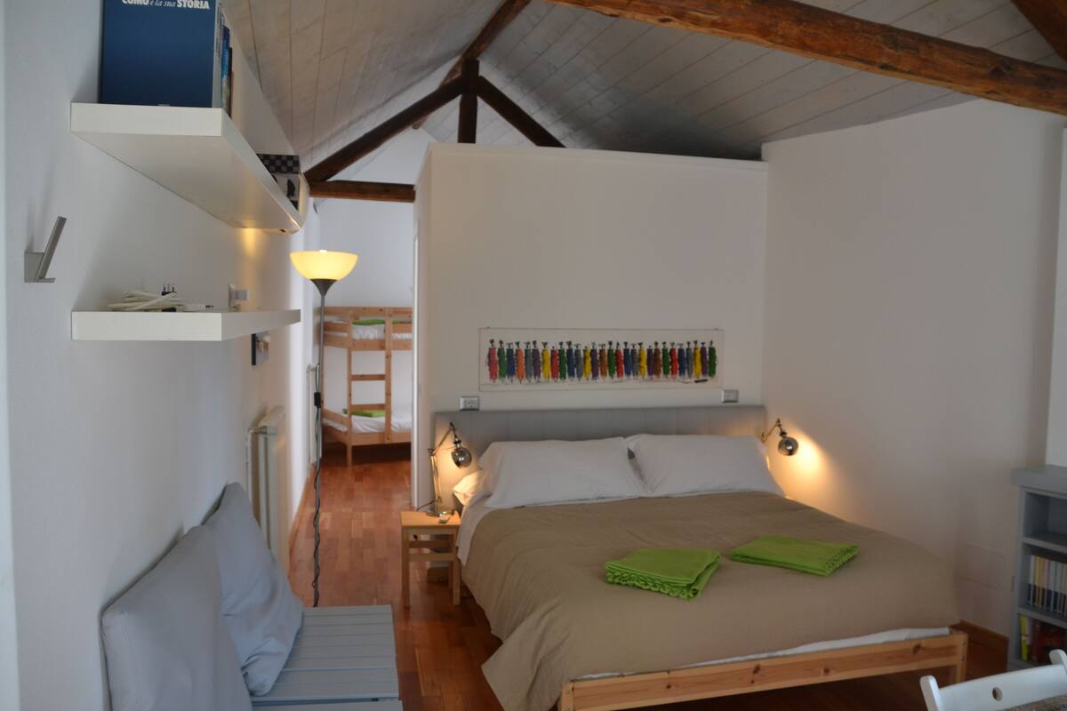 A bedroom with a wooden bed, a nightstand, a lamp, a shelf with books, and a wall-mounted picture frame.
