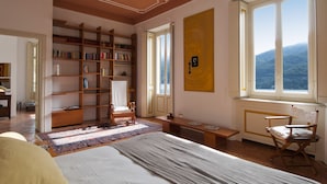 A spacious bedroom with a large bed, a wooden bookshelf, a desk, and a window with a mountain view. - Villa Nina Relais Boutique B&B (Carate Urio)