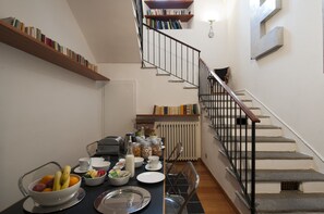 Ein Essbereich mit einem für das Frühstück gedeckten Tisch, einer Treppe und Bücherregalen.