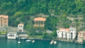 A coastal area with buildings, a dock with boats, and a hillside with dense greenery. - Villa Nina Relais Boutique B&B (Carate Urio)