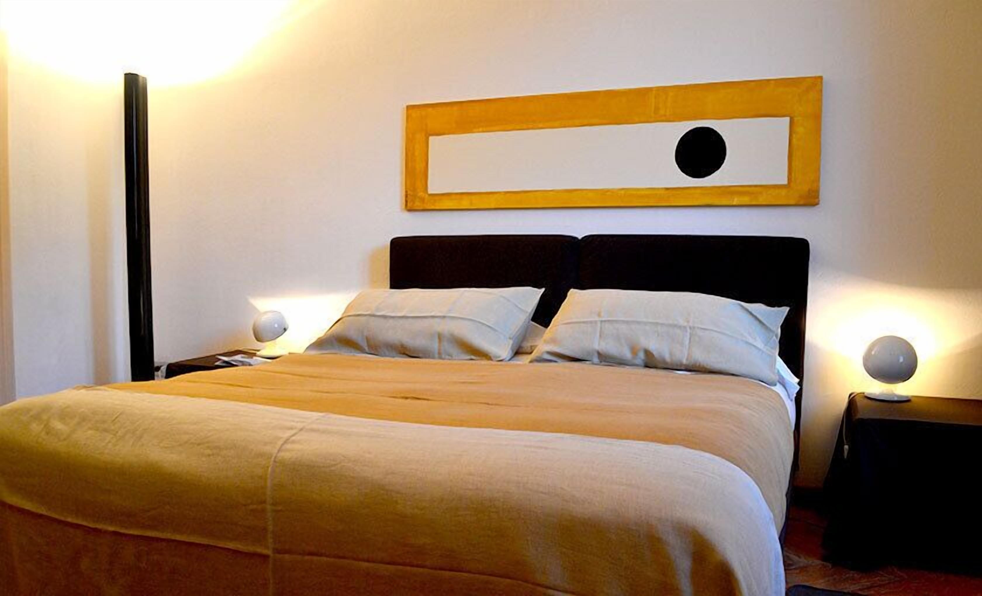 A neatly made bed with a wooden headboard, two bedside lamps, and a wall-mounted artwork.