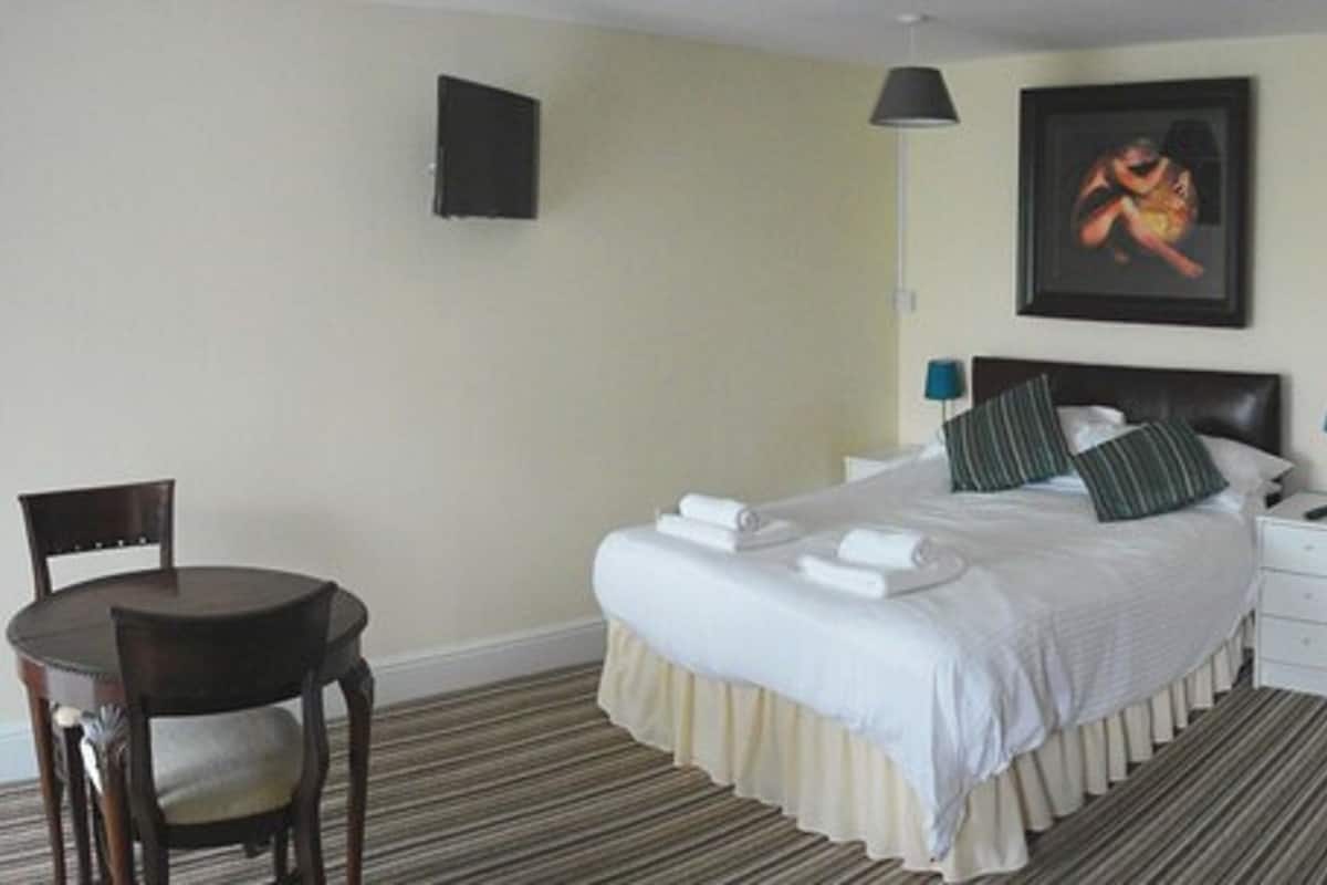 A hotel room with a bed, a chair, a bedside table, a lamp, and a painting on the wall.