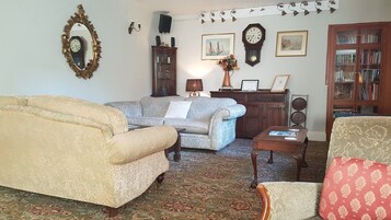 Una sala de estar tradicional con un sofá, un sillón y una mesa de centro. Hay un aparador con puertas de vidrio y un reloj en la pared.