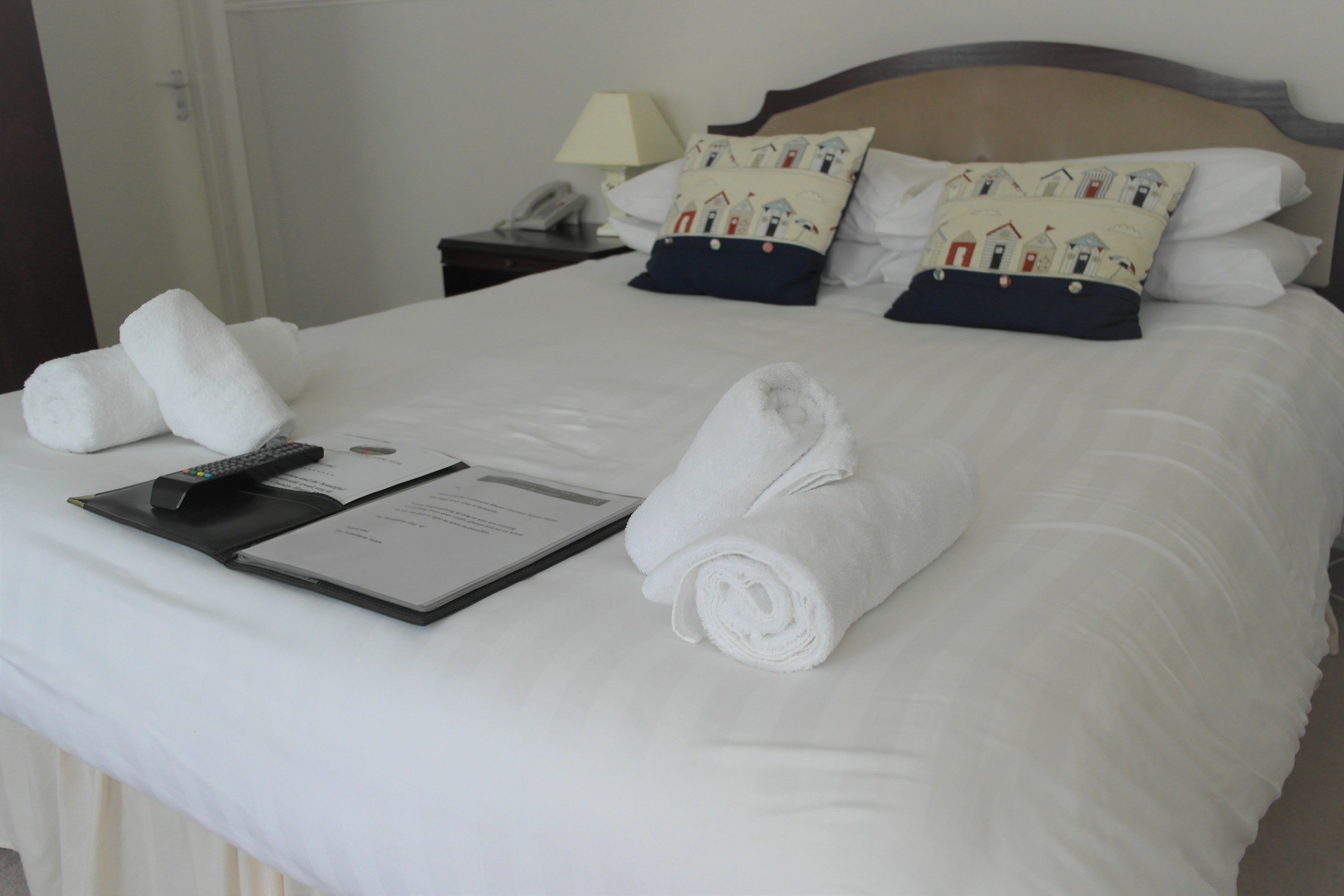 A neatly made bed with white linens, a remote control, a menu, and rolled towels.