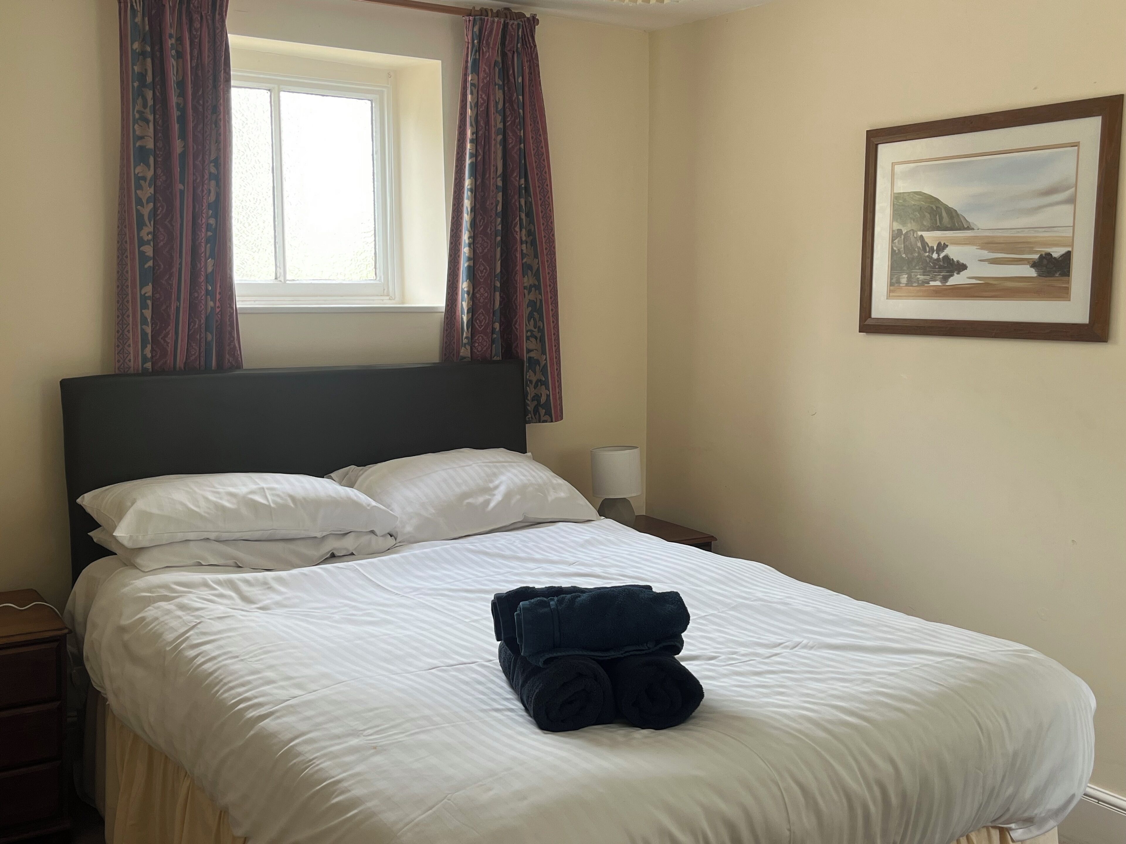 A neatly made bed with white linens, a dark headboard, and a pair of folded towels on the bed.