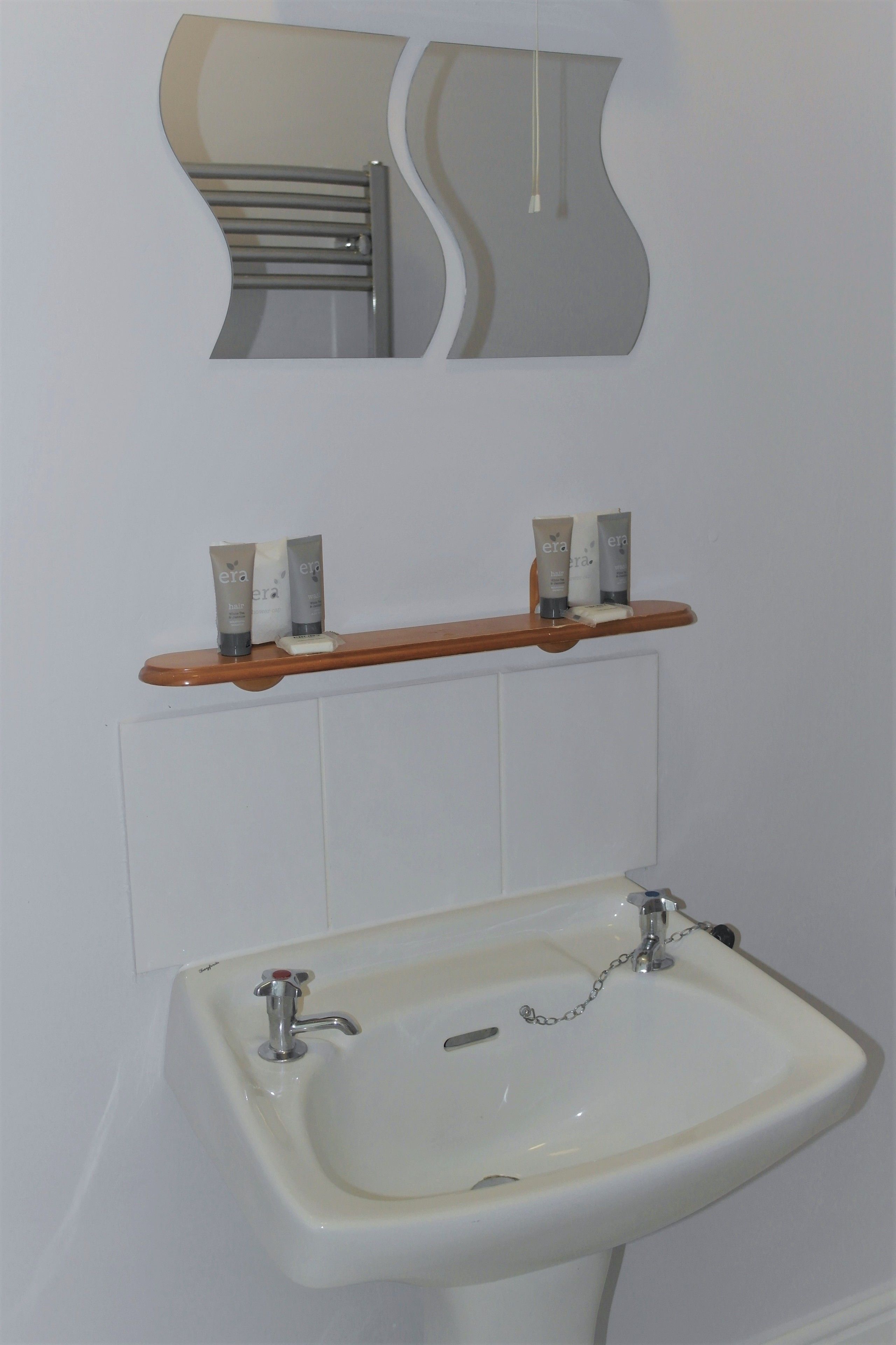 Un baño con un lavamanos blanco, un espejo y un estante con artículos de tocador.