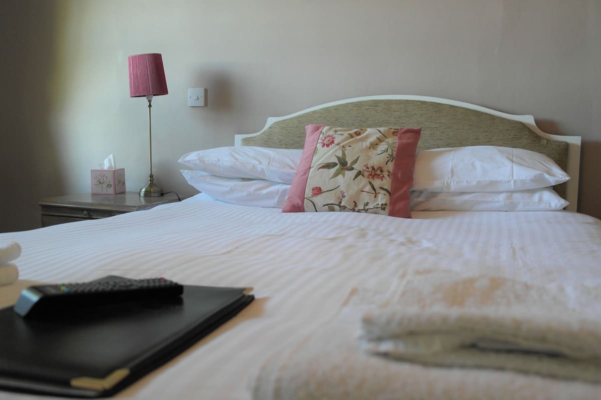 A neatly made bed with a floral pillow, a bedside lamp, and a remote control on a bedside table.