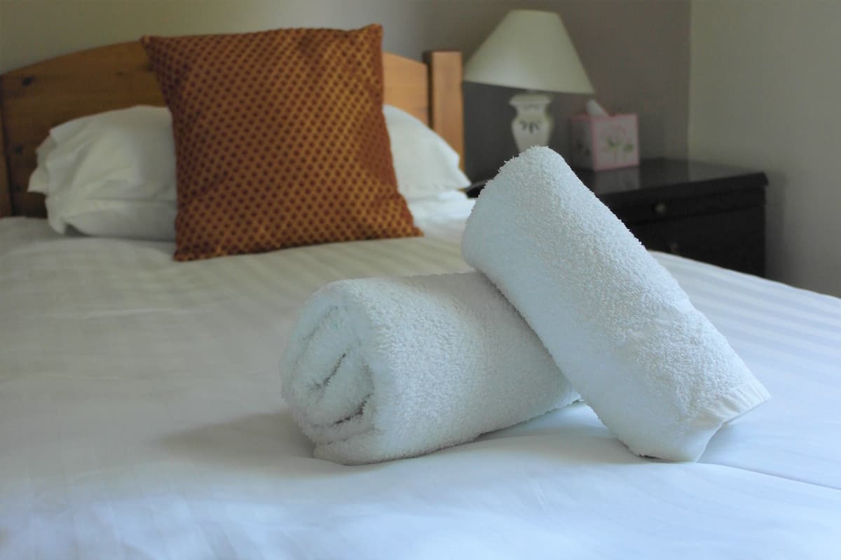 A neatly made bed with white linens and two rolled white towels placed on it.