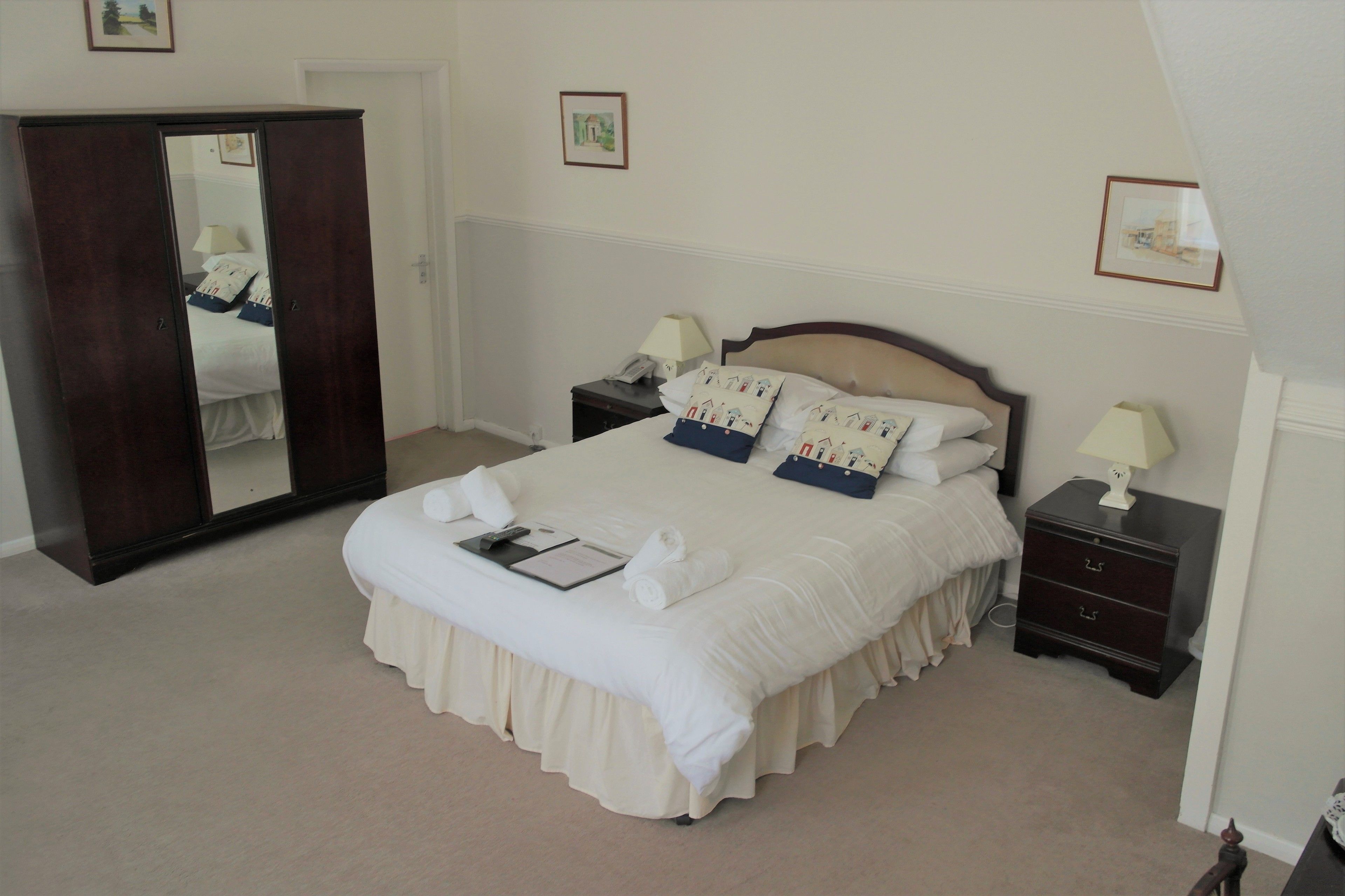 A neatly made bed with pillows, a bedside table with a lamp, a dresser, and a mirror.