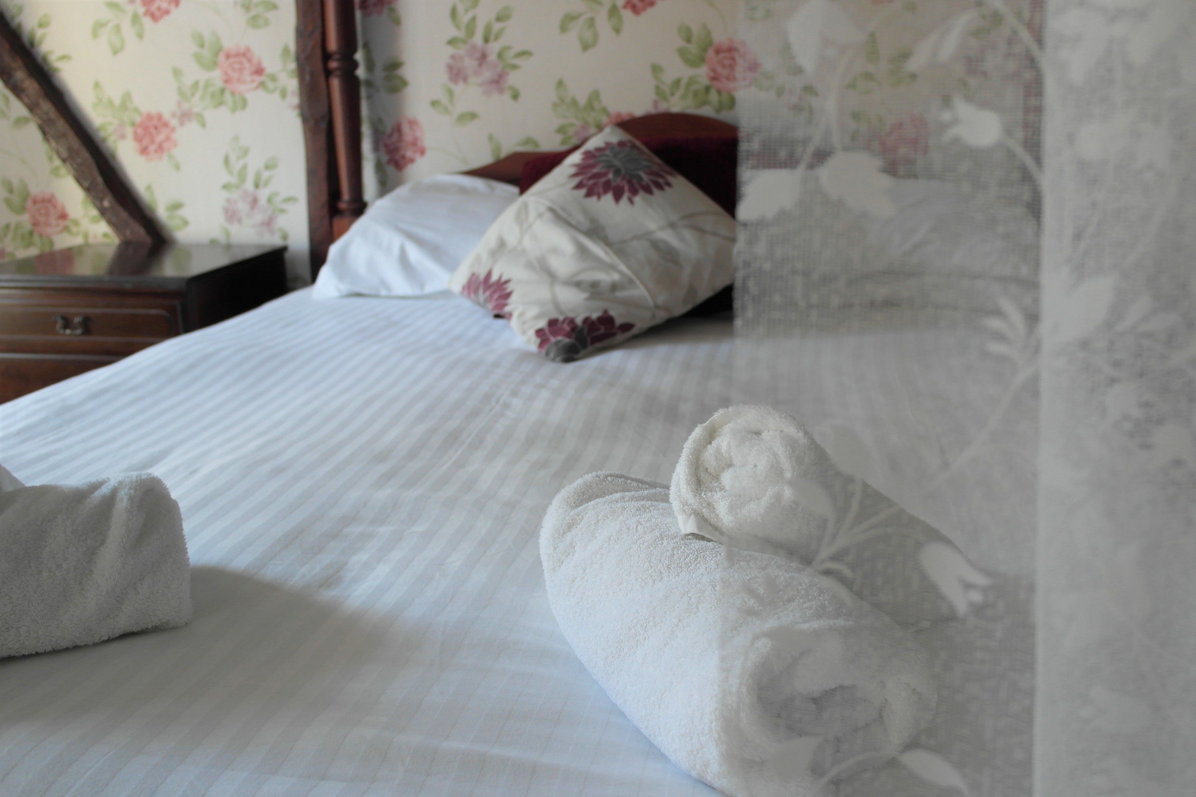 A neatly made bed with white linens and a floral-patterned headboard.