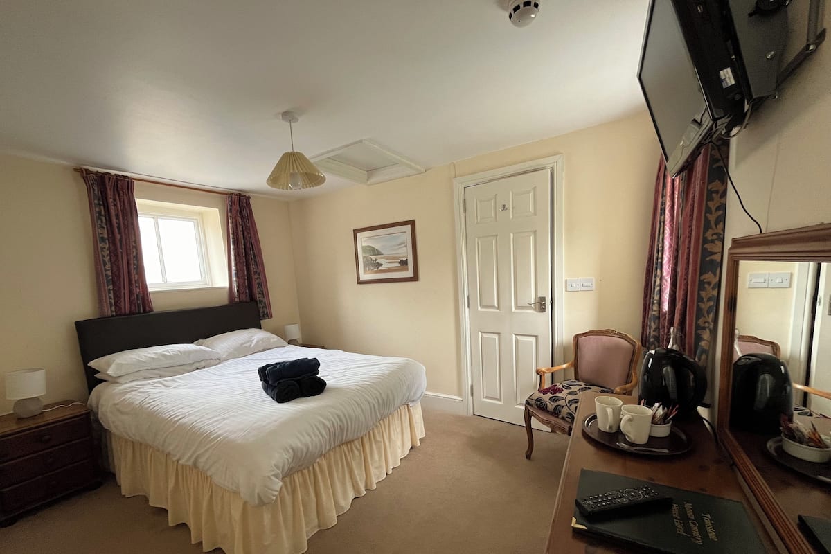 A hotel room with a bed, a desk with a coffee maker, a chair, and a television.