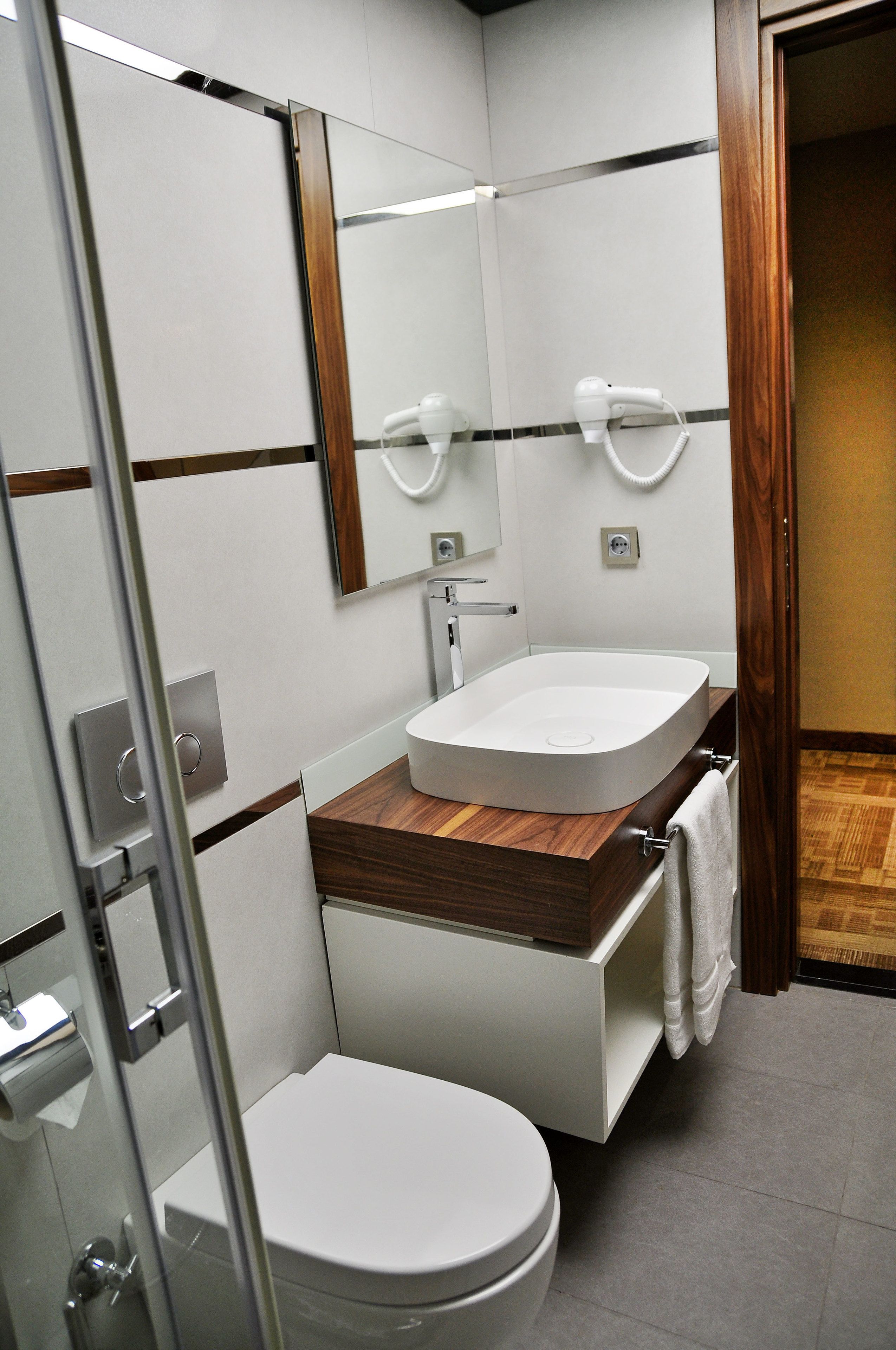 A modern bathroom with a white toilet, a wooden vanity, a white sink, and a mirror.