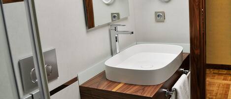 A modern bathroom with a white toilet, a wooden vanity, a white sink, and a mirror.