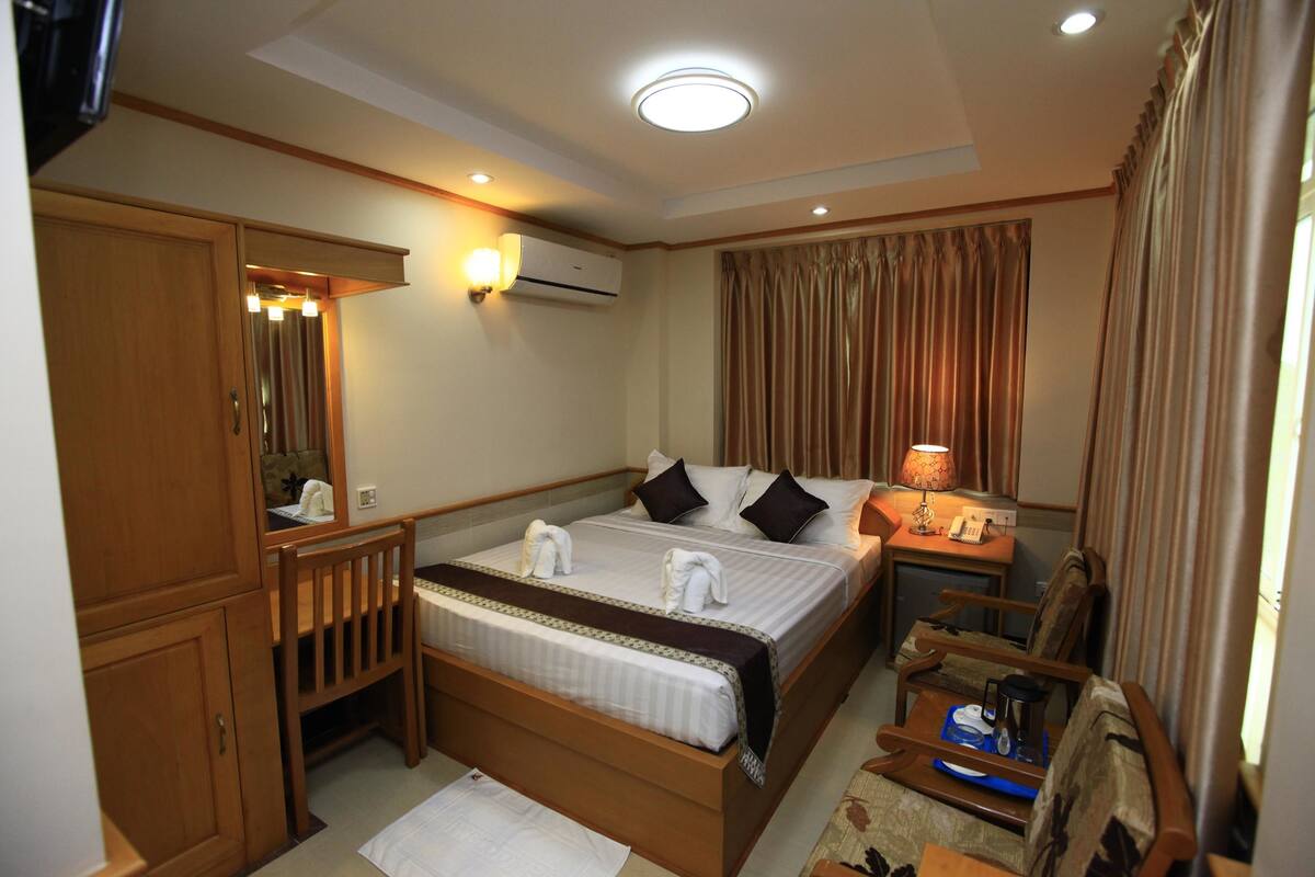 Quarto de hotel com cama, mesa de cabeceira, abajur e guarda-roupa.