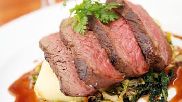 A plate of sliced steak with a garnish, served on a white plate with a sauce.